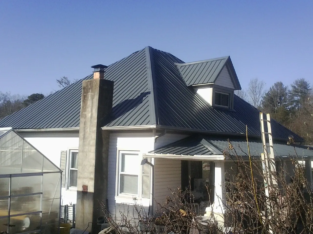 Dark blue standing seam metal roof on a white farmhouse with dormer — Slate & Tile Roof Repair by Roofing Brothers in Grant