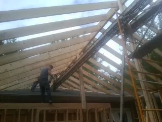 Rafters going up over a new addition with a worker on the wall in Grant