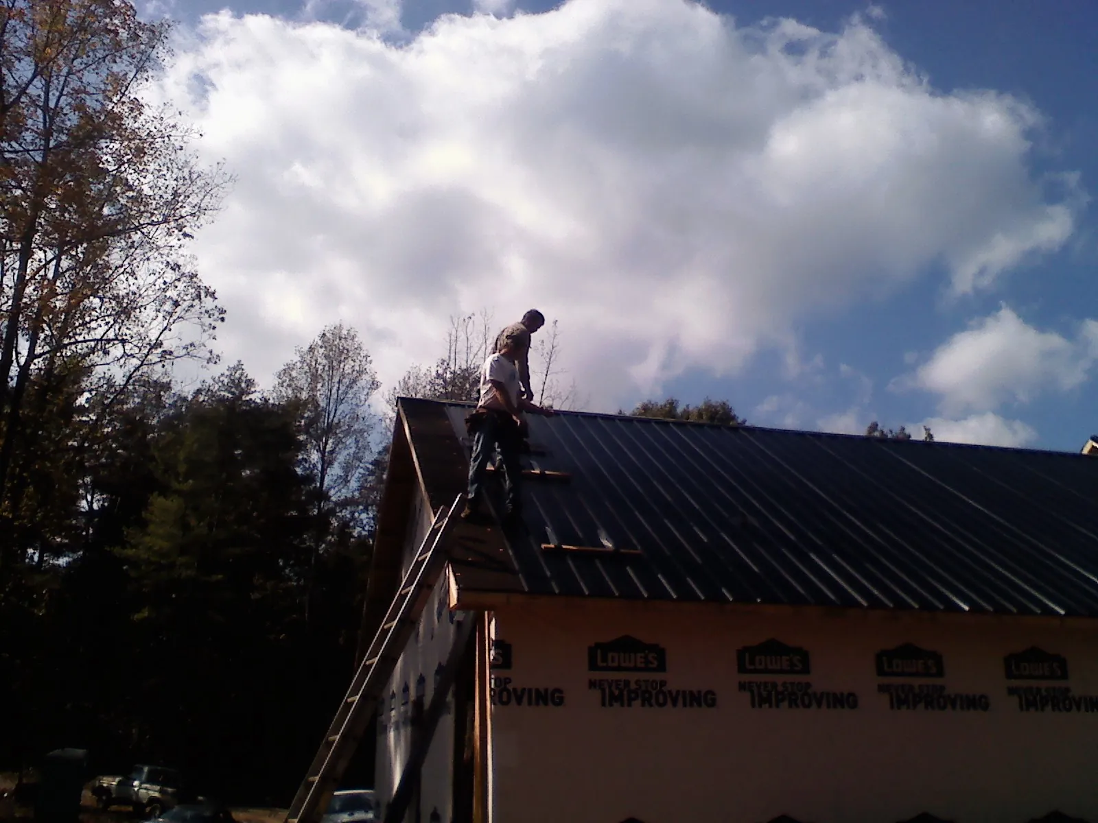Roofer fastening dark metal panels high against a cloudy sky, from a Roof Inspection job in Grant