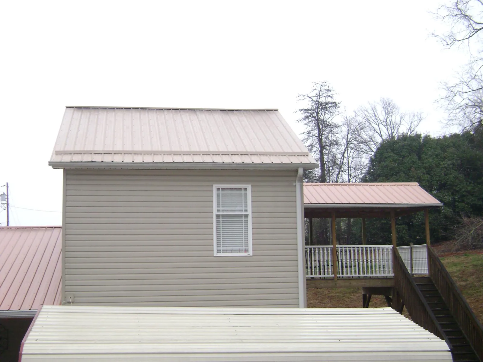 Tan metal roofs on a two story addition and attached porch, from a Roof Replacement job in Grant